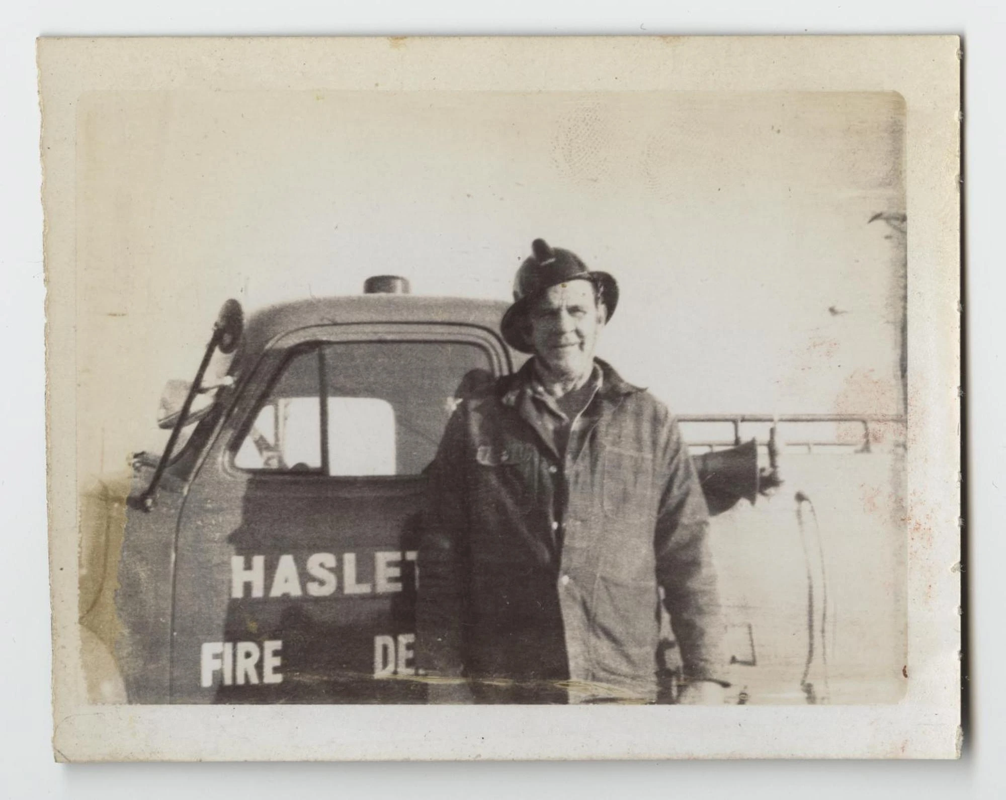 A smiling man in a firefighter's helmet and heavy coat stands beside a fire truck door lettered "Haslet Fire Dept."